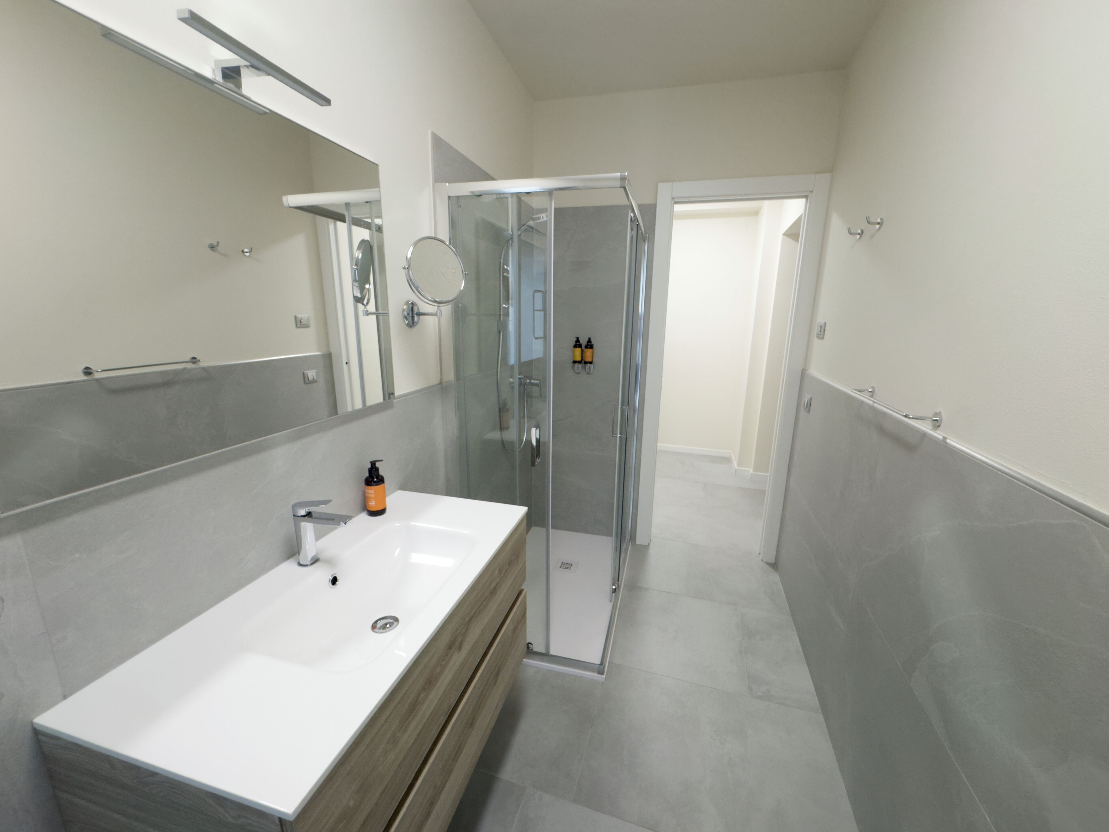 Un baño moderno con ducha envuelta en vidrio, un lavamanos blanco y un mueble de tocador de madera.