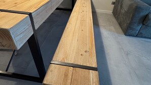 A wooden dining table with benches, a grey sofa, and a wall clock.