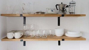 A kitchen with two wooden shelves holding various glassware and dishes. - GuestReady - Charming 3-Bedroom Apartment in NW11 (London)