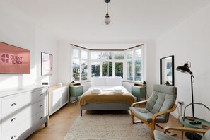 A bedroom with a bed, a chair, a desk, a lamp, and a window with a view of buildings. - GuestReady - Charming 3-Bedroom Apartment in NW11 (London)