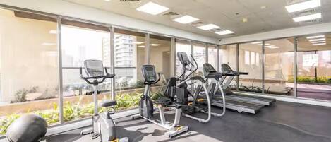 A gym with exercise equipment, large windows, and a view of buildings outside.
