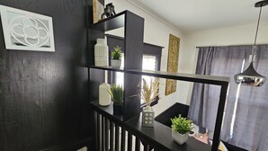 Un soggiorno moderno con una scala in legno scuro, uno specchio con cornice nera e una pianta in vaso sul pavimento.