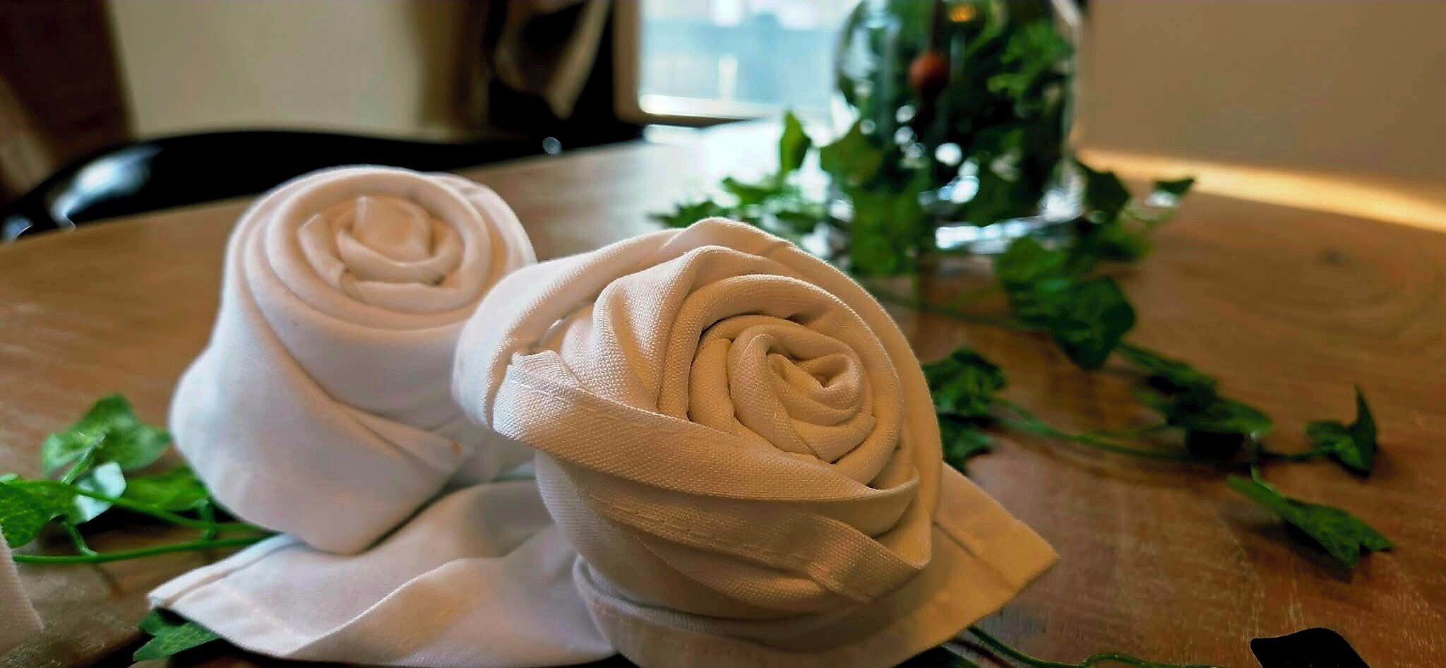 Two rolled towels on a wooden table with green leaves.