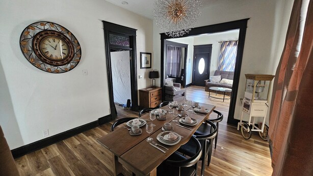 Zona pranzo con tavolo di legno apparecchiato per quattro persone, un orologio decorativo a parete e un lampadario.