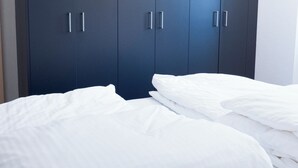 Et soveværelse med en stor, mørk garderobe, to senge med hvidt sengetøj og en loftlampe.