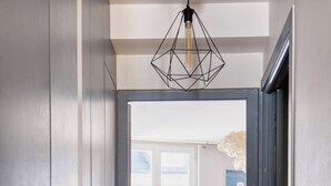 Corredor que leva a um quarto com cama, um quadro e uma luminária geométrica.