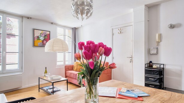 Uma sala de estar moderna com uma mesa de centro de madeira, um vaso com tulipas cor-de-rosa, um sofá rosa e uma janela grande.