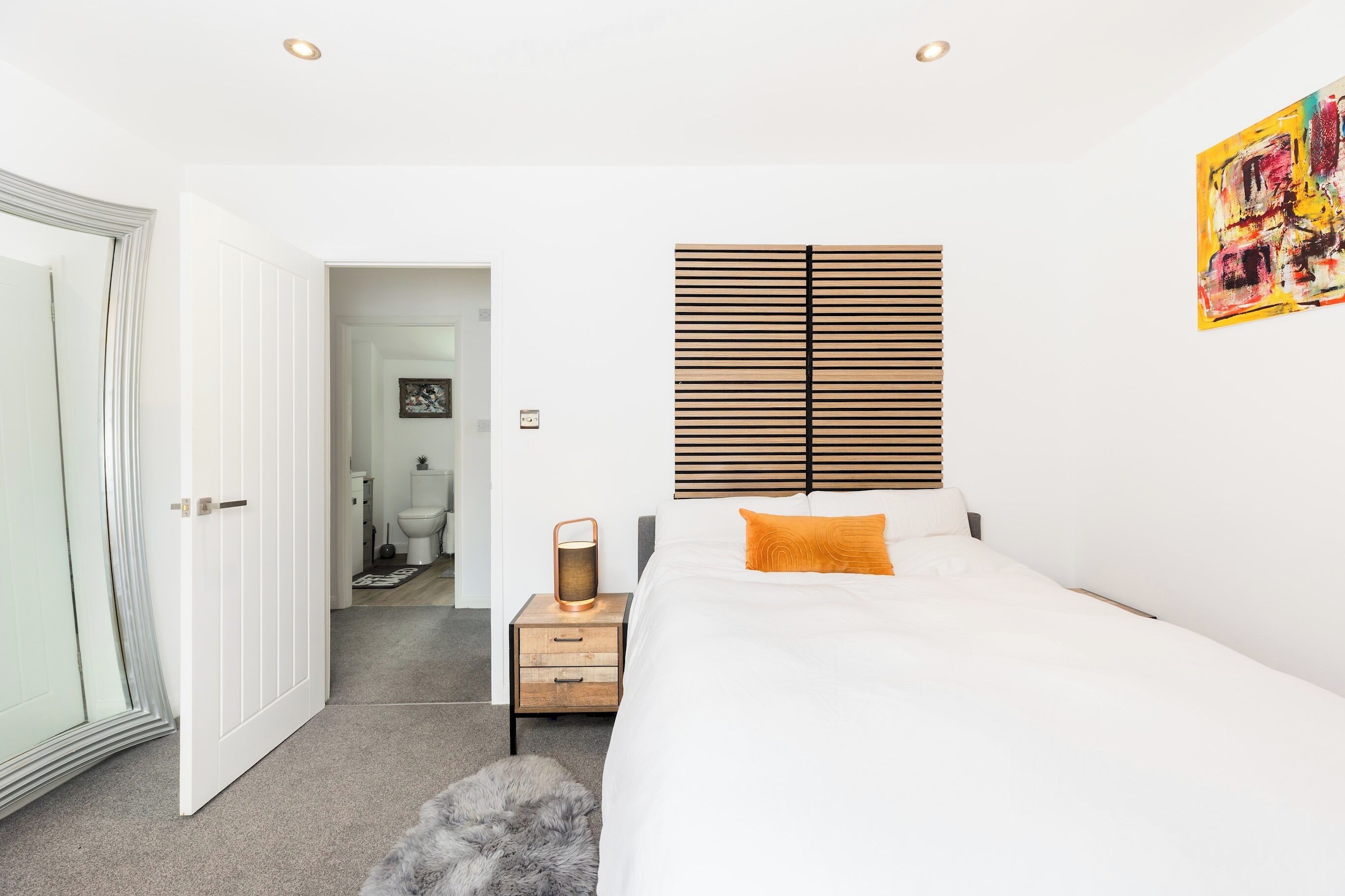 A bedroom with a bed, bedside tables, a nightstand, a radiator, a door, and a wall with a painting.