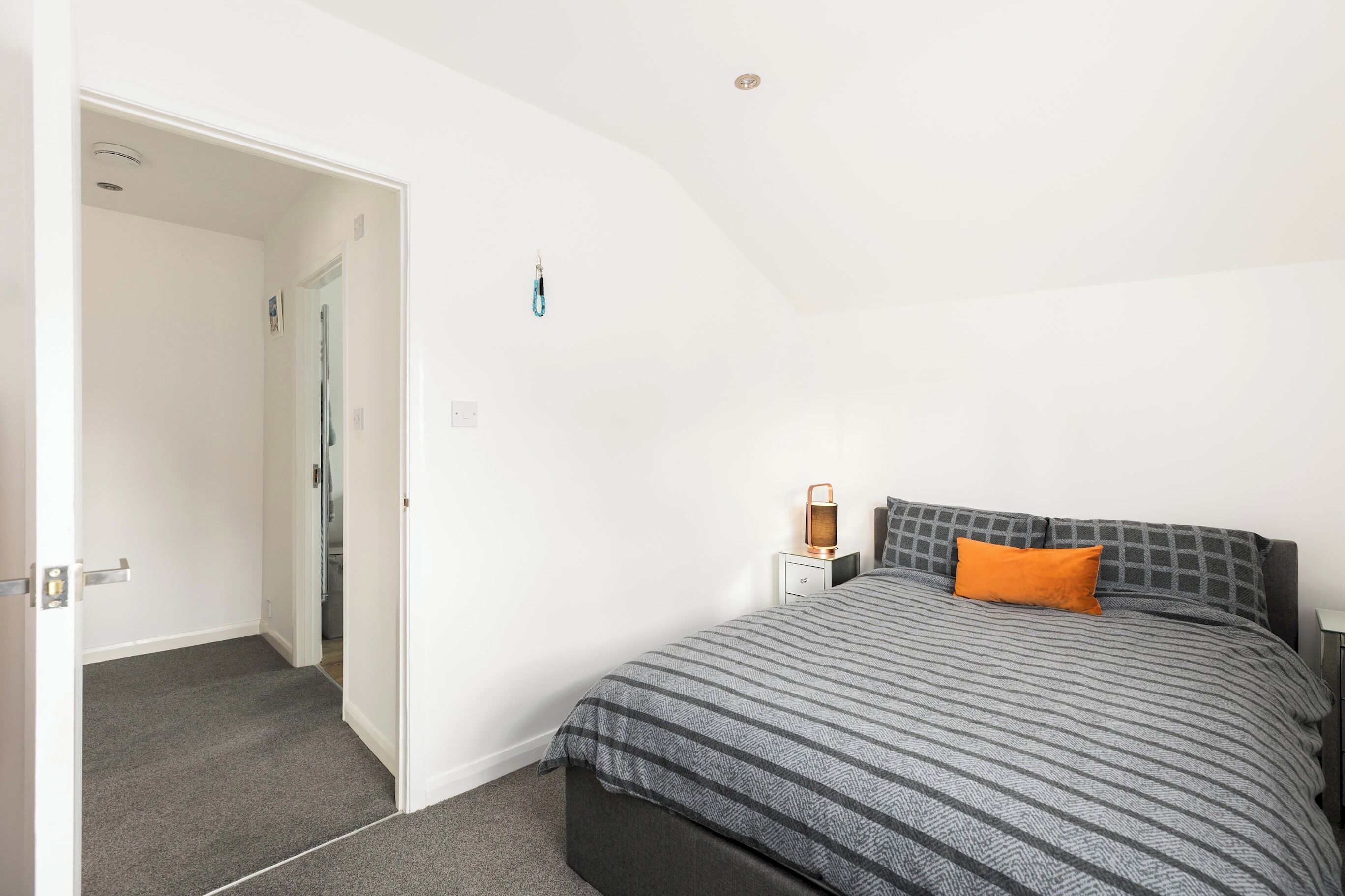 Une chambre à coucher avec un lit, un oreiller orange, une table de chevet et une lampe fixée au mur.