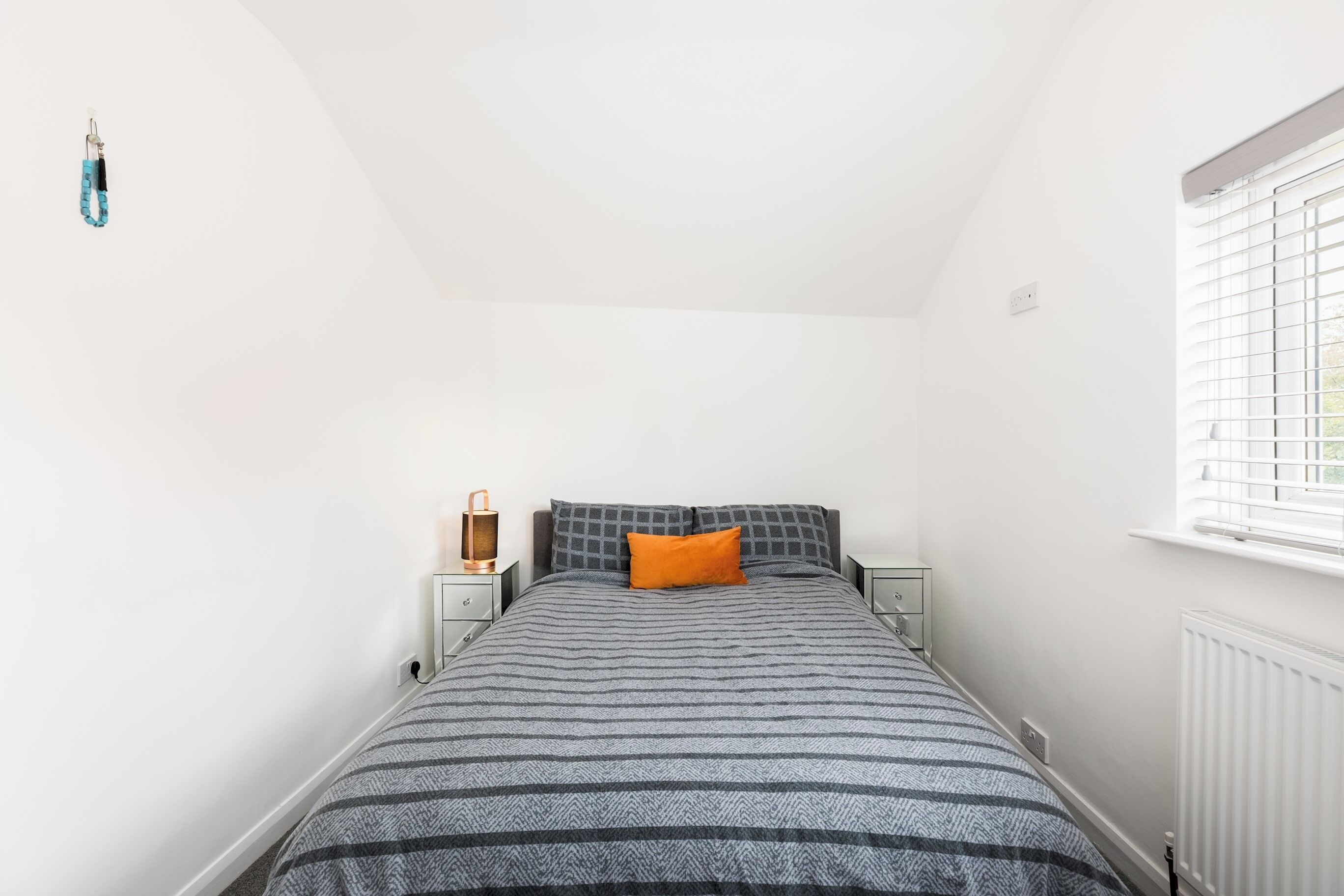 A bedroom with a bed, two bedside tables, a lamp, and a window with blinds.