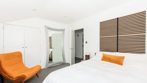 A modern hotel room with a large bed, an orange armchair, a mirror, and a wooden headboard. - Stylish & Modern 2 Bed with Parking - Pass the Keys (Stratford-upon-Avon)
