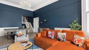 Ein Wohnzimmer mit einer Couch, Sesseln, einem Couchtisch und einer Treppe, die auf einen Balkon führt.