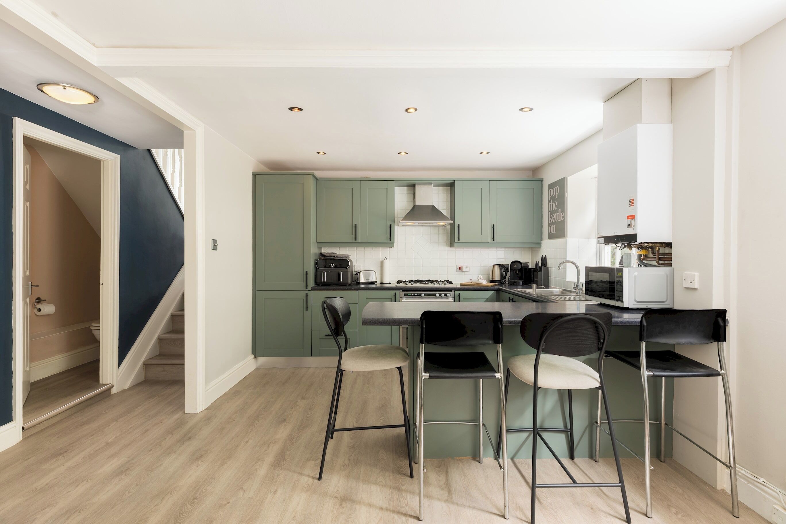 A modern kitchen with green cabinets, a central island with bar stools, and a staircase leading to a second floor.