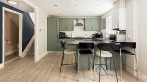 Eine moderne Küche mit grünen Schränken, einer zentralen Kochinsel mit Barhocker und einer Treppe, die zu einer zweiten Etage führt.