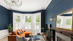 Ein Zimmer mit blauer Wand, Kamin, großem Spiegel und einem Fenster mit Rollläden.
