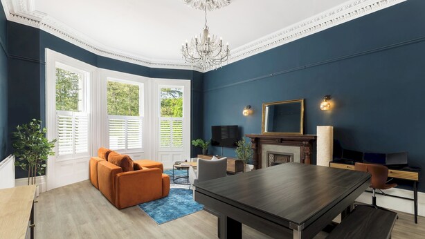 Ein modernes Wohnzimmer mit einer dunkelblauen Akzentwand, einem großen Holzesstisch, einem Kamin und einem bequemen orangefarbenen Sofa.