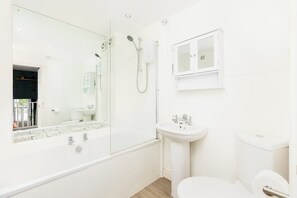 Un baño moderno con ducha envuelta en vidrio, lavamanos pedestal y retrete.