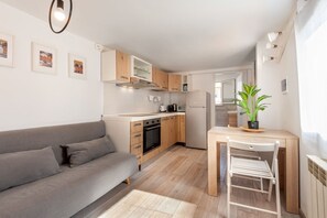 Ein gemütlicher Wohnbereich mit Küchenzeile, einer Couch, einem Esstisch mit Stuhl und einem Blumentopf.