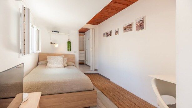 Een slaapkamer met een bed, nachtkastje en een bureau met een computer.
