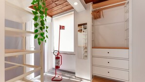 Een kamer met een houten plafond, witte wanden, een witte dressoir en een rode brandblusser, plus een hangplant.