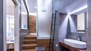 A modern bathroom with a wooden staircase, a glass shower enclosure, and a large mirror above a sink. - GuestHost - Spacious and charming 50 square meters studio apartment, perfect for three people, located on the first floor of a building (NO elevator).The property is located in the central area of ​​Salerno (limited traffic zone), a neighborhood well (Salerno)
