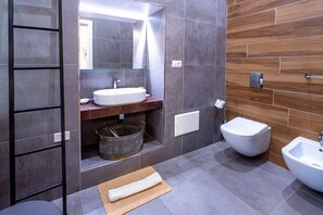 Un baño moderno con un espejo grande, un lavabo, un bidé y una toalla en el suelo.