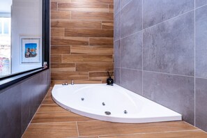 A modern bathroom with a freestanding bathtub, wooden floor tiles, and grey wall tiles.