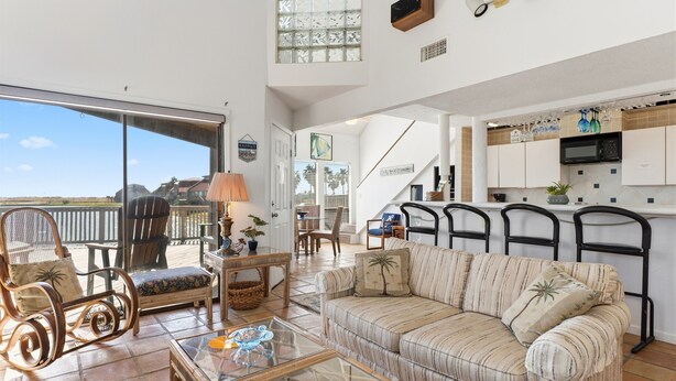 A spacious living area with a sofa, chairs, a glass coffee table, and a view of the outdoors. - Coastal Lagoon Retreat in Matagorda  w/ Beach Views & Pool Access (Matagorda)