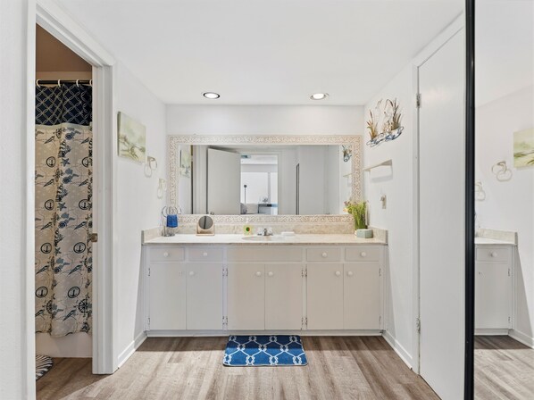 Un baño con un espejo grande, muebles blancos, un lavabo y zona de ducha.
