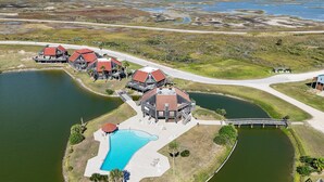 An aerial view of a coastal property with multiple houses, a large swimming pool, and a dock. - Coastal Lagoon Retreat in Matagorda  w/ Beach Views & Pool Access (Matagorda)