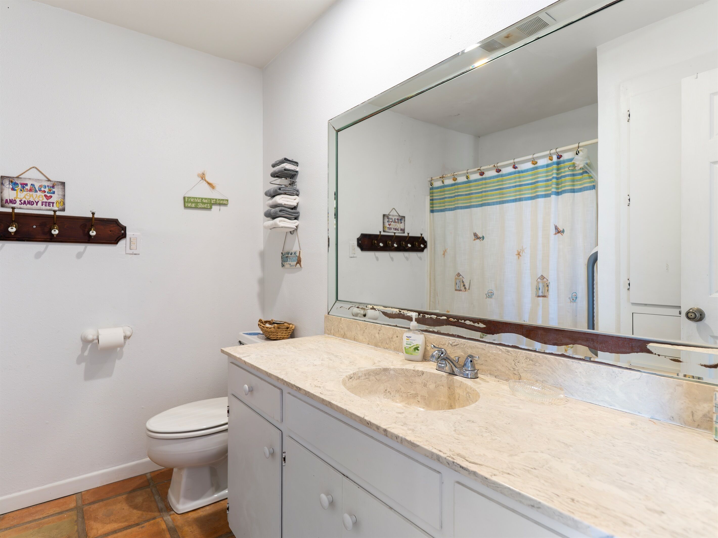 A bathroom with a toilet, sink, and mirror. There are towels and a basket on the wall.