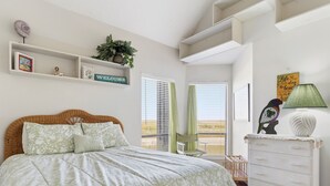 A bedroom with a bed, a dresser, a chair, a window with blinds, a wall-mounted shelf with a plant, and a welcome sign. - Coastal Lagoon Retreat in Matagorda  w/ Beach Views & Pool Access (Matagorda)