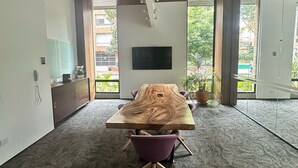 Een moderne vergaderzaal met een grote houten tafel, paarse stoelen, een wandgemonteerde televisie en grote ramen met uitzicht op groen.