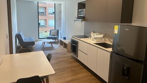Een kleine keuken met een koelkast, spoelbak en magnetron. Er is een eethoek met een tafel en stoelen.