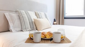 Una cama bien hecha con almohadas, una bandeja de cruasanes y dos vasos de jugo de naranja.