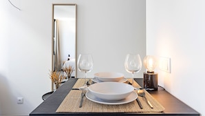 Una mesa de comedor dispuesta con platos, cubiertos y copas de vino, con una lámpara y un espejo al fondo.