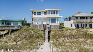 Una casa fronte spiaggia su due piani, con un portico in legno e una scala che conduce all'ingresso.