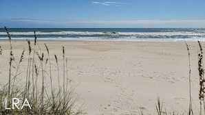 Una spiaggia con sabbia e onde, e un po' d'erba sullo sfondo.
