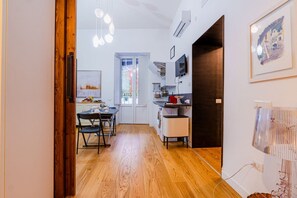 A modern kitchen with wooden flooring, a dining area with chairs, and a view through a glass door to an outdoor area.
