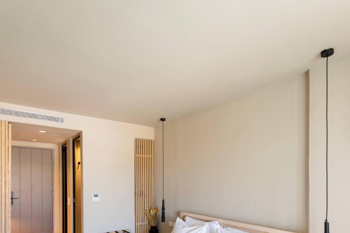 A neatly made bed with white linens and black accents, a bedside table with a lamp, and a wooden door.
