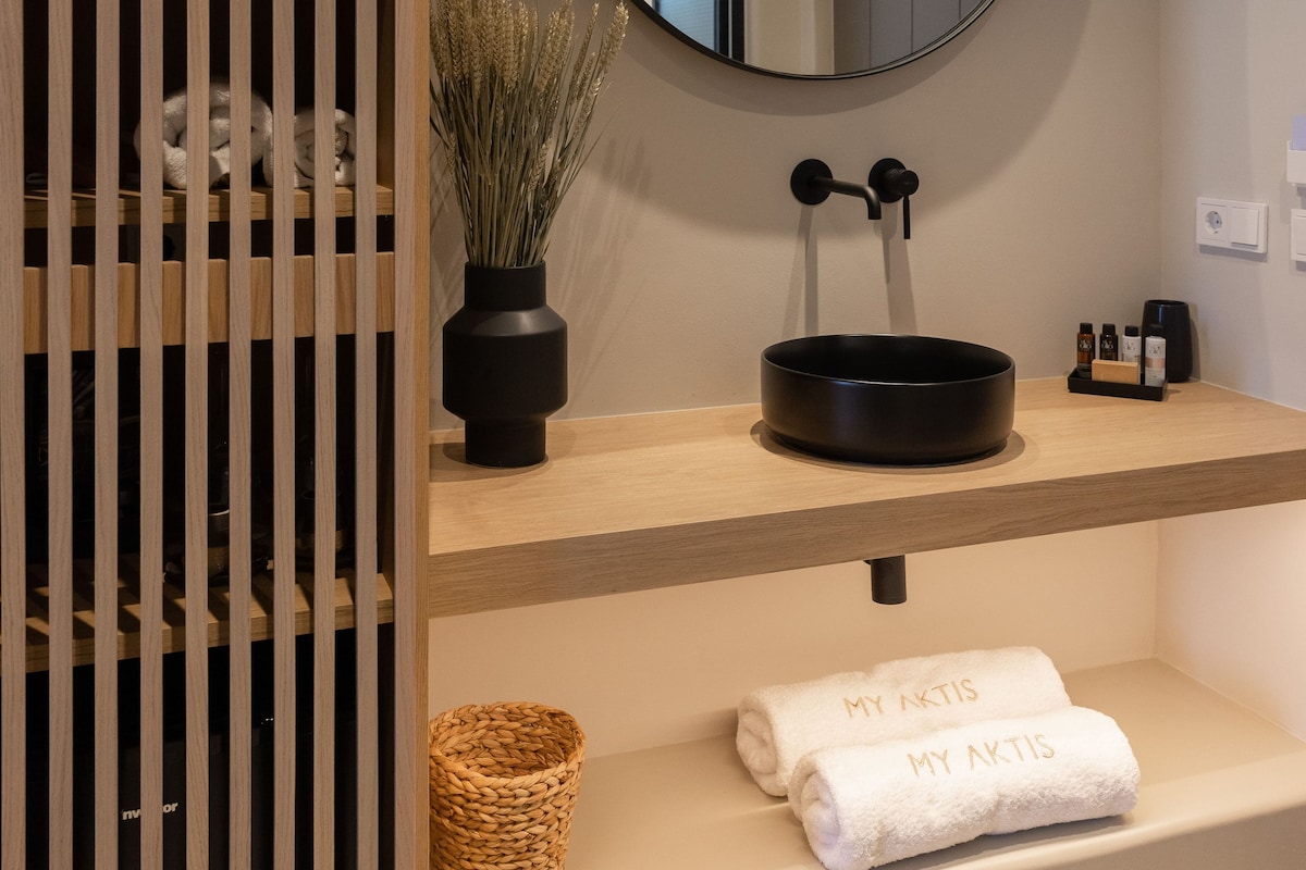 A bathroom with a round mirror, a black sink, a towel rack, and a wooden partition.