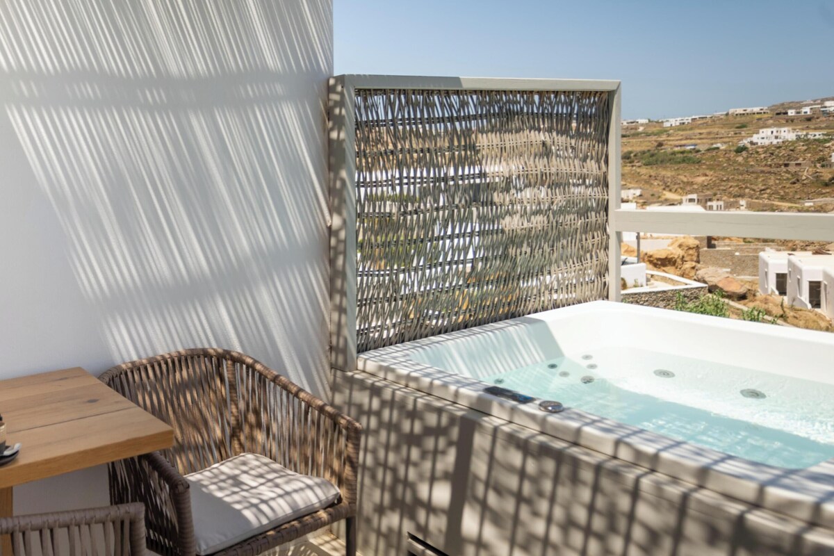 Een balkon met een jacuzzi, rieten meubels en een tafeltje met kop en schotel.