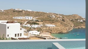 A coastal view with buildings on a hillside, a clear sky, and a swimming pool. - Hotiday Mykonos South Coast (Mykonos)