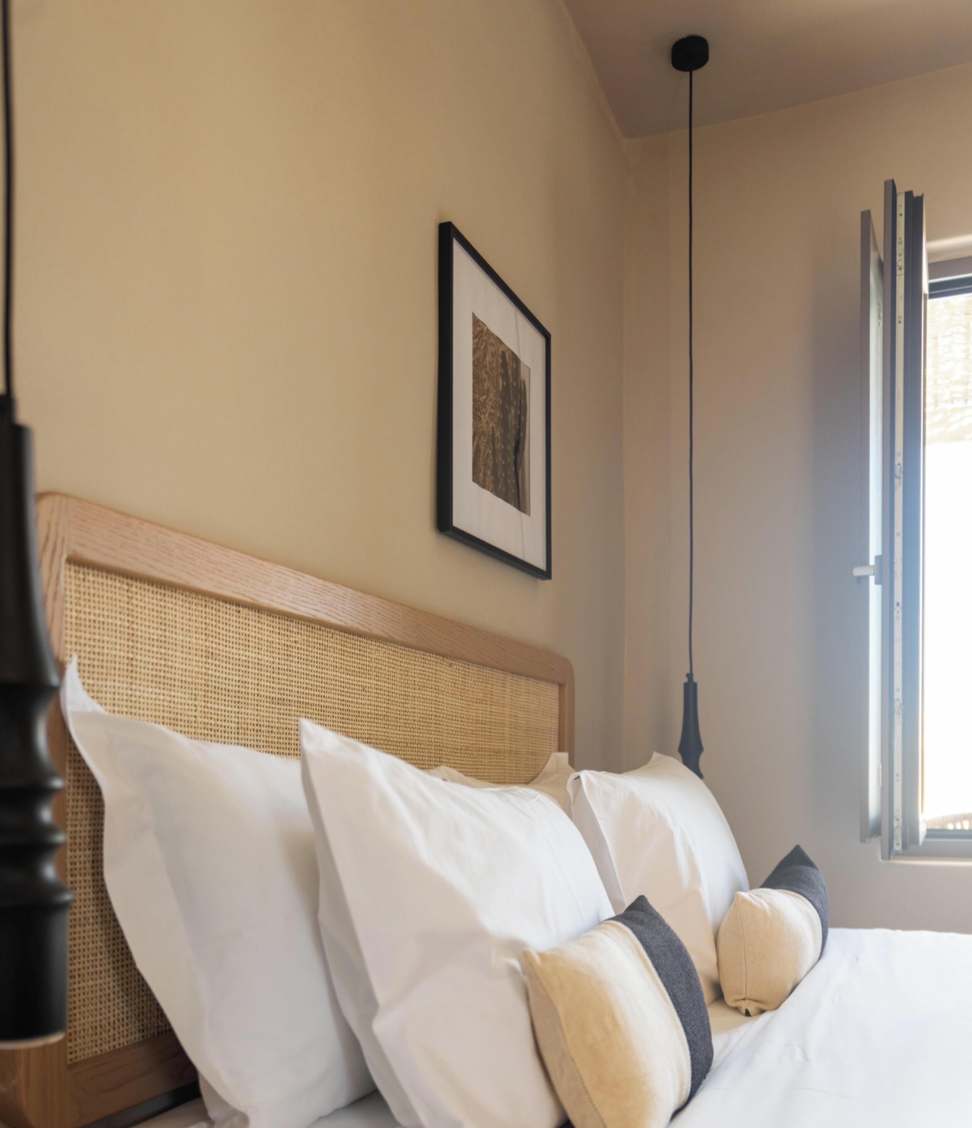 A bed with white bedding, a woven headboard, and a framed picture on the wall.