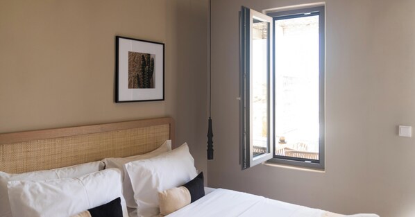 Une chambre à coucher avec un lit, des oreillers, un tableau encadré et une fenêtre dont le volet est ouvert.