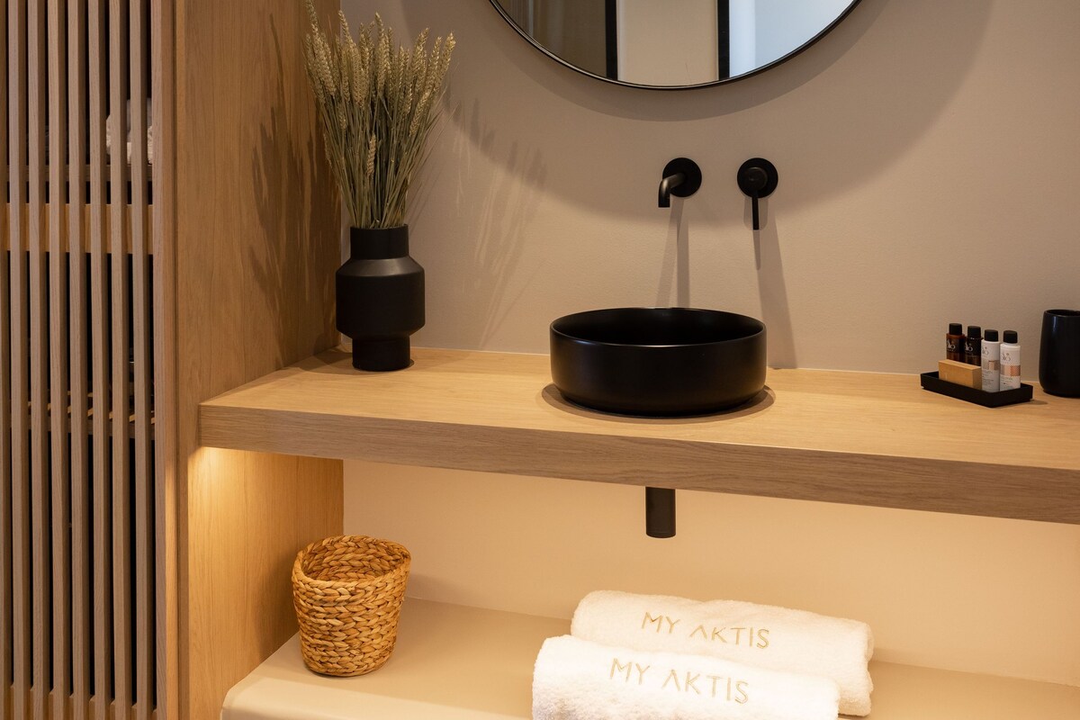A bathroom with a round mirror, a black sink, a potted plant, a woven basket, and a towel with text.