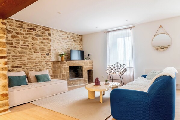 Un salon avec un mur en pierre, une cheminée, un canapé, un fauteuil bleu et un téléviseur.
