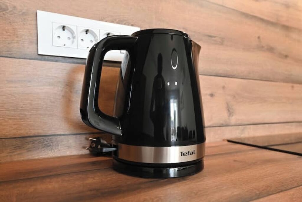 A black Tefal electric kettle on a wooden surface with a power outlet in the background.