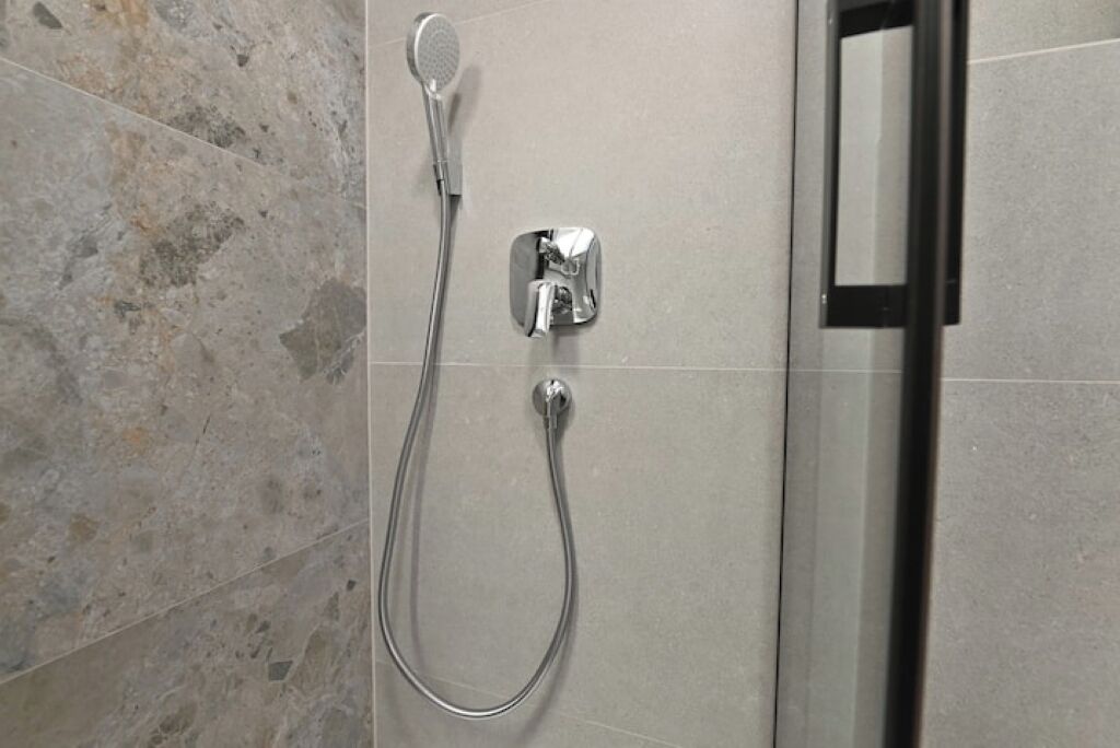 A shower with a handheld showerhead and a wall-mounted control panel.