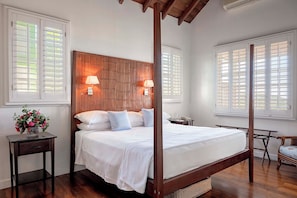 A four-poster bed with a wooden headboard, two bedside lamps, and a nightstand with a vase of flowers. - Tamarind Villa, Montpelier Nevis (Charlestown)